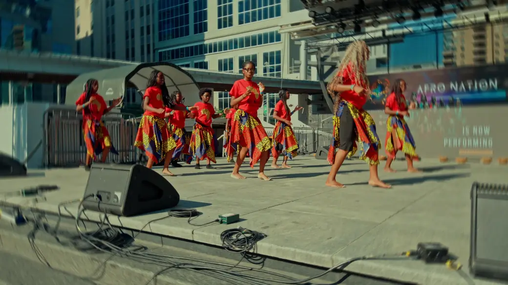 An African dance troupe in red tops and patterned skirts performs on stage