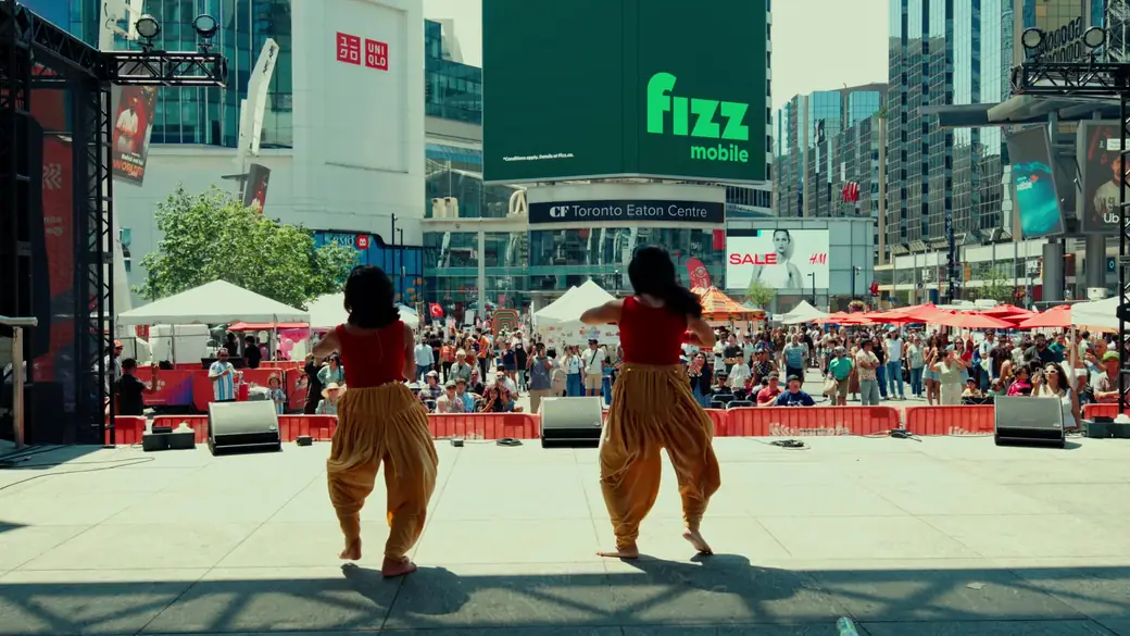 Two dancers in gold trousers perform facing the crowd, the Eaton Centre behind them