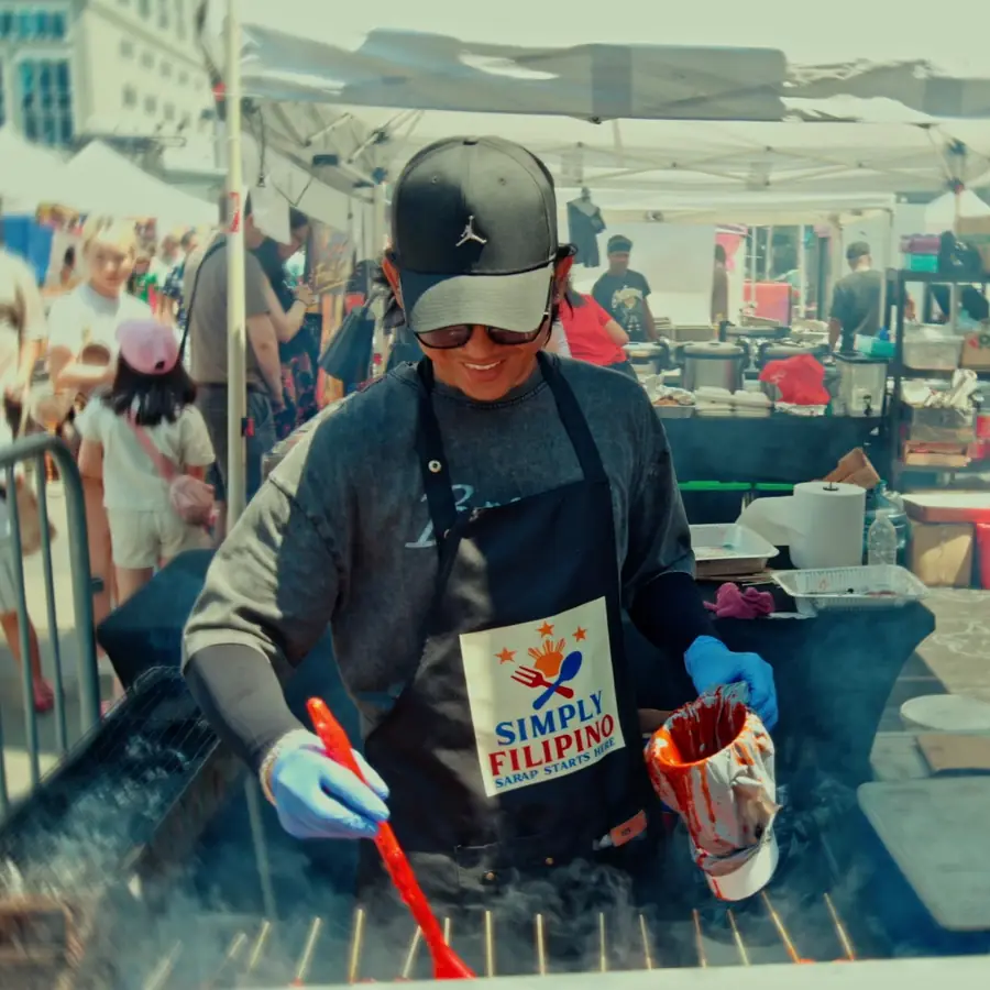 A cook in a Simply Filipino apron grills skewers at a WorldFest food stall