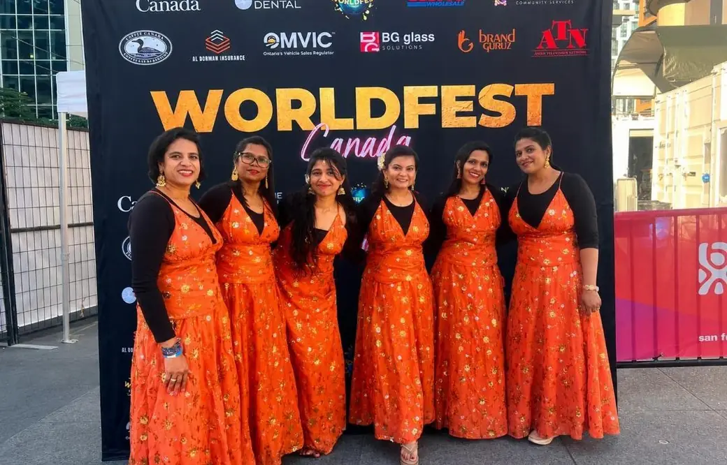 Performers in orange dresses pose at the WorldFest sponsor media wall