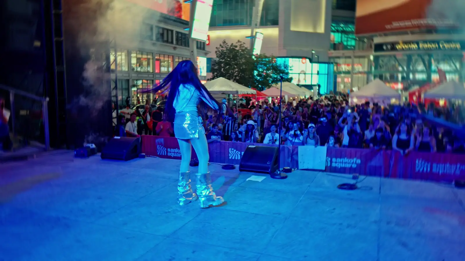 A singer in silver performs to a packed night crowd at Sankofa Square under blue stage lights