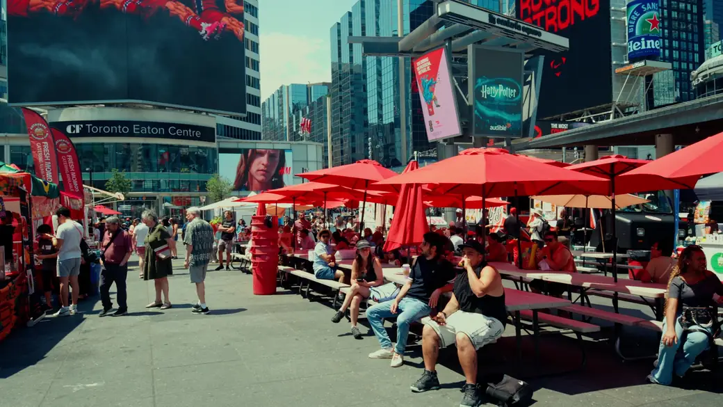 Festival-goers eat at picnic tables under red umbrellas across from the Eaton Centre