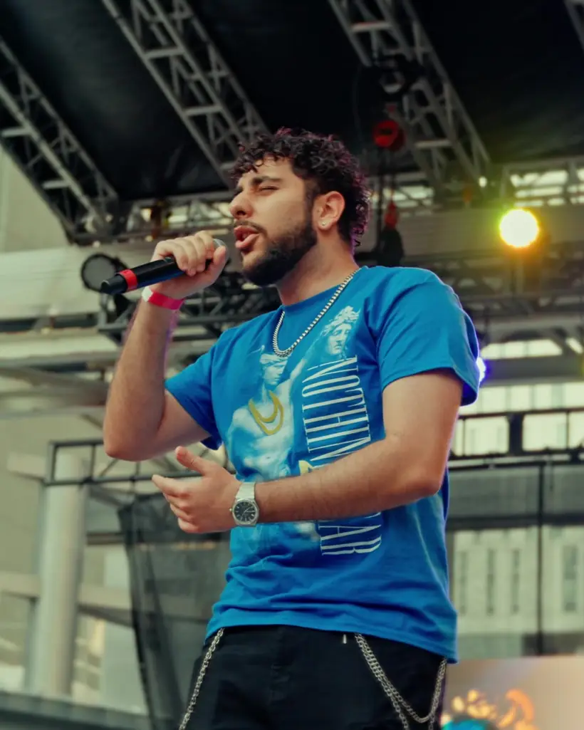 A singer in a blue T-shirt performs under stage lights at dusk
