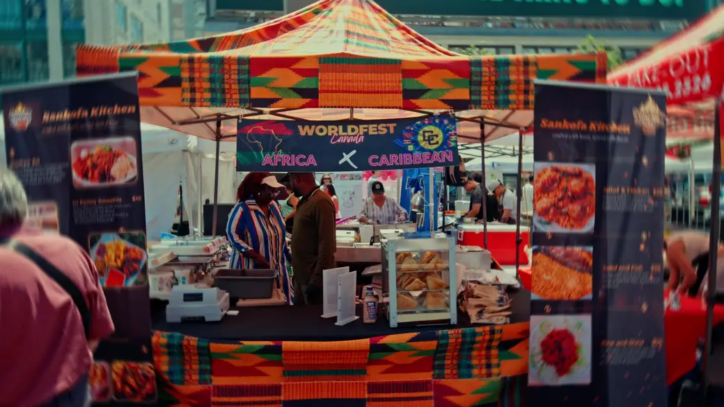 A food stall with a WorldFest Africa × Caribbean banner and a kente-pattern canopy