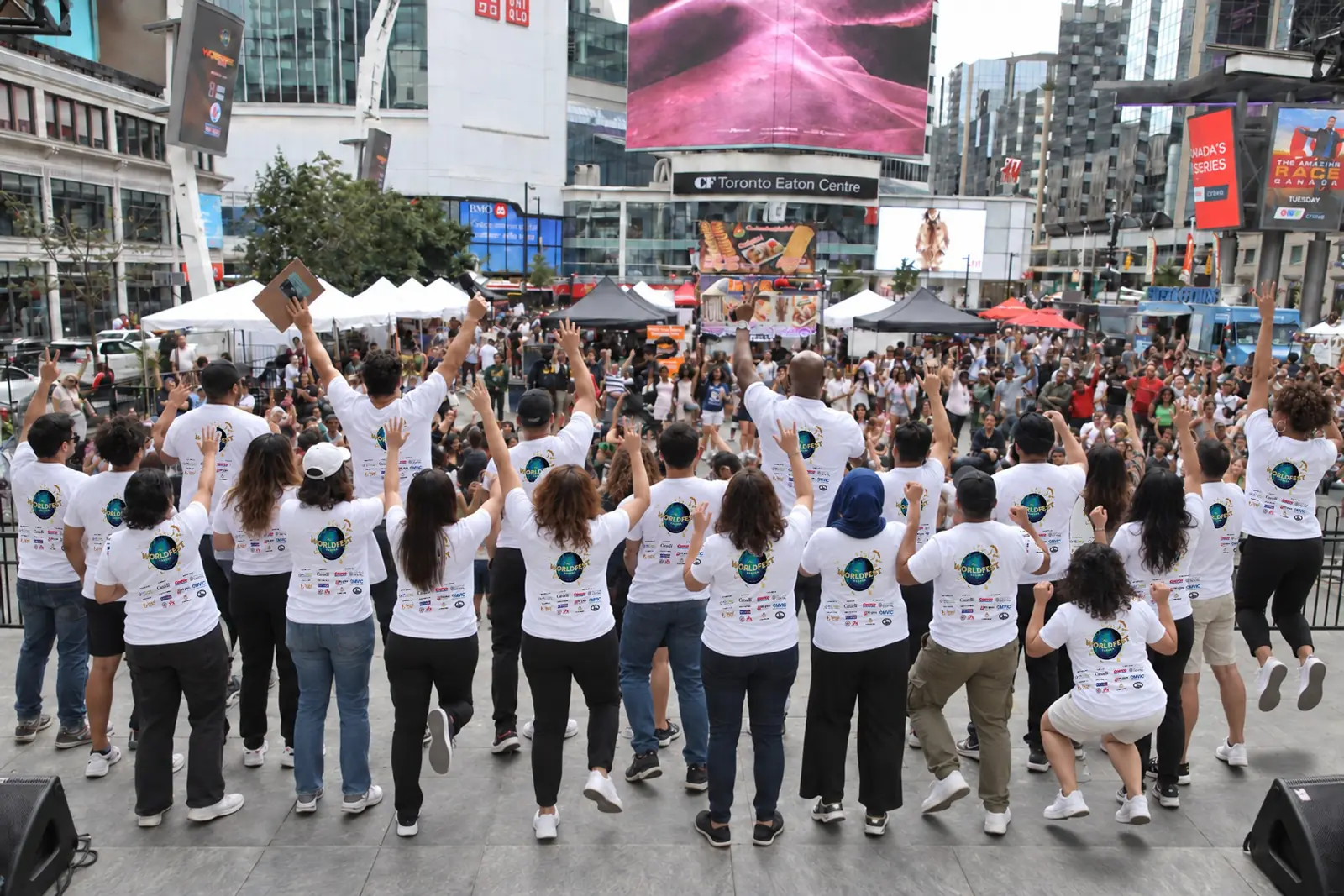WorldFest volunteers in festival T-shirts cheer on stage, facing the crowd at Sankofa Square